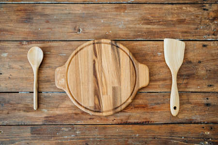 High-quality kitchen utensils. A round textured plate of light wood is located on the table,a spoon...