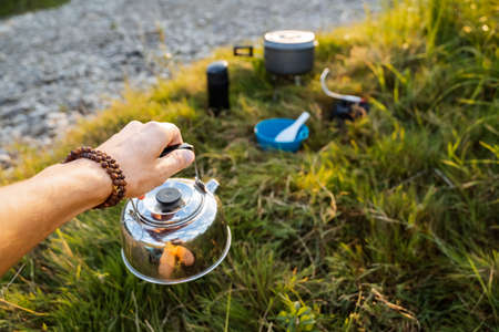 Kettle of silver color to hold in your hand against the background of nature. Tourist breakfast....