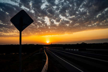 Incredibly beautiful sunset in the countryside. Bright peach and orange sunset and cumulus clouds in the sky. Sunset on the highway, the shadow of the road sign. High quality photoの写真素材