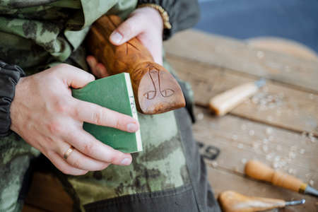 A man in a camouflage uniform treats the surface of a wooden toy. Souvenir made of wood in the form...
