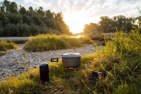 Sunset, dawn on a rocky bank by the river with a camping pot , a horizontal frame. Meal on a hike, tourist food. Outdoor activities, summer hikes. High quality photoの写真素材