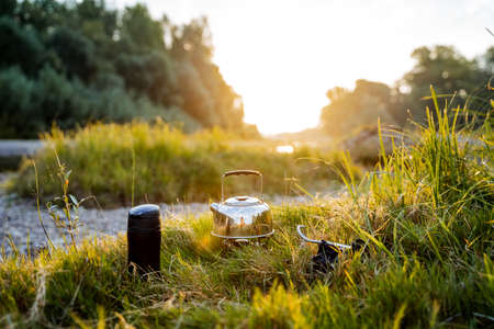 A close shot of a kettle and a flask by the river bank in the grass. Dinner in nature, meal of a tourist. Hike to nature to the river. Kettle and flask. High quality photoの写真素材