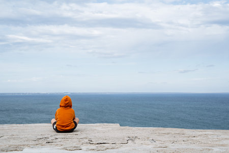 A man sits in the frame, facing the sea. Minimalistic shot of man and the sea. Bright clothes, calm sea. Time alone. PRogulka by the sea. High quality photoの写真素材