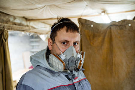 Carpenter in his woodworking workshop. Carpenter in special clothes and a mask from dust. Portrait of a worker, artisanの写真素材