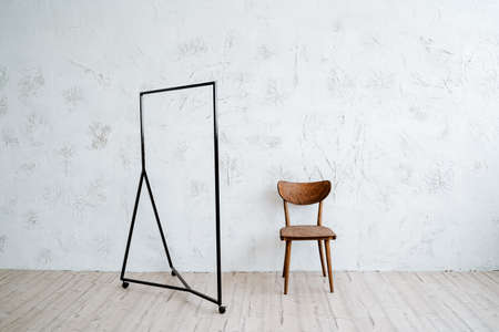 Metal hanger floor on a minimalist background. Rack for clothes on wheels. Nearby is a vintage wooden chair. Light walls, wooden floor in the room. High quality photoの写真素材