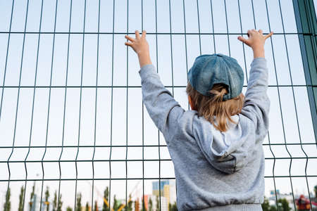 A little boy grabbed a fence on the playground. The boy watches the rides. Amusement park for...
