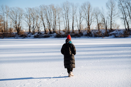 A young girl walks on a frozen lake. Panoramic view of the lake in winter. Bright cold sun. Nature walk in winter weather. High quality photoの写真素材
