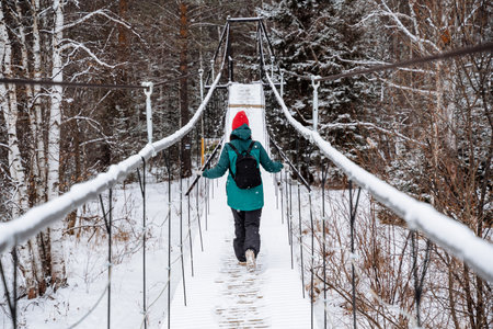 A man walks on a suspension bridge over a frozen river. Walk in winter through the forest more...
