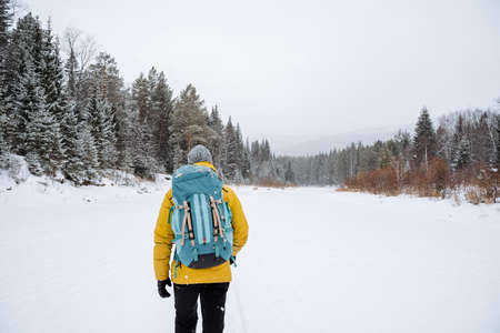 joyful traveler with a bright backpack walks through the forest expanses. Snowy forest and rocks....