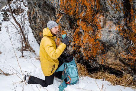 A traveler drinks tea from a by the rock. Rock climbing in winter. A journey into the mountains to the wilderness. Resting in the mountains. High quality photoの写真素材