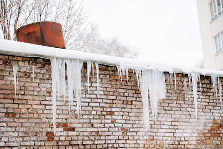 Ice icicles hang on the roof, the danger of ice falling on the head. A place of increased danger to life. The threat of snow falling from the roof. High quality photoの写真素材