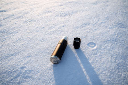 The bottle lies on the snow. The shadow of the dishes falls on the snow. A hot drink of coffee is...