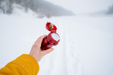 Red bottle with lid open. Hold a bottle for tea in your hand. Close-up shots against the background of snow. High quality photoの写真素材