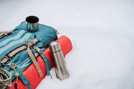 A tourist backpack lies on the snow, a red mat is fastened on the side, a bottle  is next to it.の写真素材
