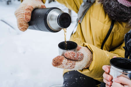 bottle in hand pour tea into a mug. A person pours hot tea from a bottle into a cup in the cold.