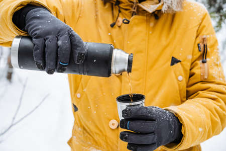 bottle in hand pour tea into a mug. A person pours hot tea from a bottle into a cup in the cold.の写真素材