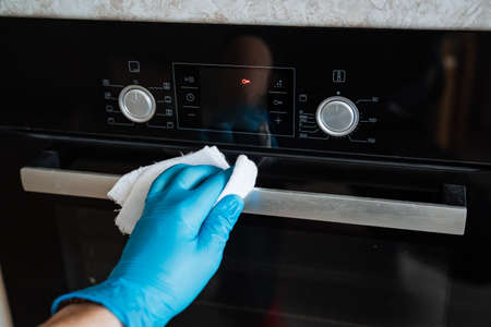 Wipe the gas stove with a rag. Cleaning the house. A blue glove holds a white rag. Wash the metal...