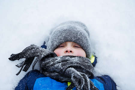 Portrait of happy little boy is lying in a snowdrift. Winter fun, playing with snow. pure snow. high quality photoの写真素材