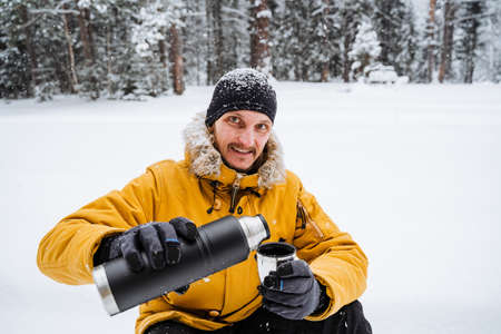 Smiling and happy traveler pours and drinks hot tea or coffee from thermos.Snowy forest and rocks. Climbing the mountain in winter. Survival in the wild. high quality photoの写真素材