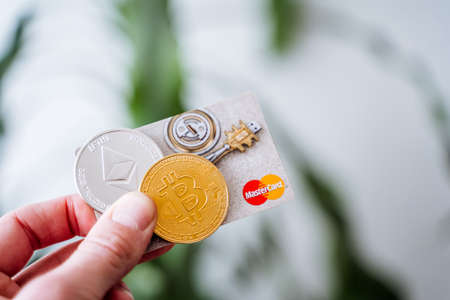 Russia Ufa February 2022: MasterCard accepts cryptocurrency. The hand holds bitcoin and a plastic card. Payment coin on the Internet. virtual money. high quality photoのeditorial素材