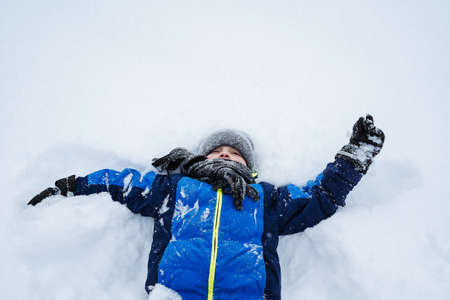 A happy little boy is lying in a snowdrift. Winter fun, playing with snow. pure snow. high quality photoの写真素材