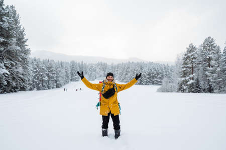 Smiling and happy traveler with hiking backpack on his back. Snowy forest and rocks. Climbing the mountain in winter. Survival in the wild. High quality photoの写真素材