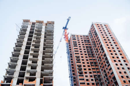 Panoramic view of two newly built houses opposite each other. A construction crane lifts concrete...