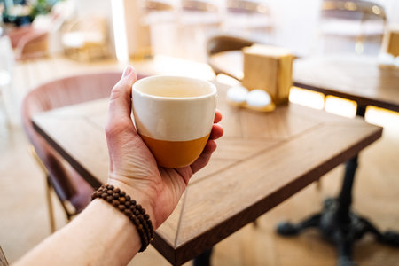 A hand holds a mug of tea in front of the cafe. Drink a hot drink at the table in the restaurant. Glass in hand bracelet, thumb. Aroma of masala tea. high quality photoの写真素材