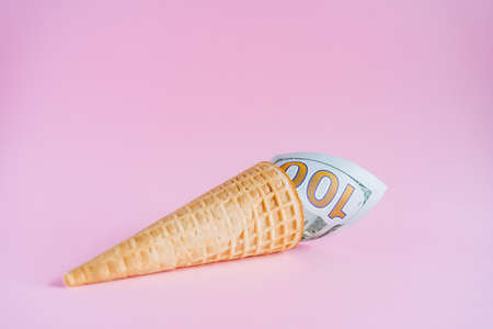 A hundred dollars in an ice cream cone. Unusual ice cream with a bill. A horn with money on a pink...
