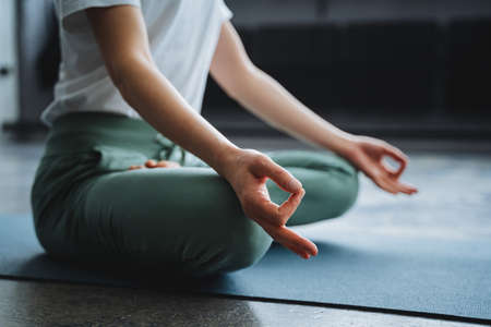 A young girl sits in the lotus position of her hand on her lap, her fingers folded into the rank of mudra. Time of Zen, immersion inward, solitude, alone at home, tranquility and peaceの写真素材
