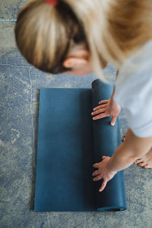 A view from above of a girl rolls out a yoga mat. Prepare for meditation, spread the carpet on the floor with your hands. Blue color fitness accessory. high quality photoの写真素材