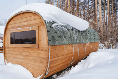 The bath barrel stands in nature under a layer of snow. Long wooden sauna made of boards. A window...
