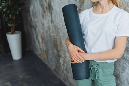A girl holds a yoga mat in her hands Close-up photo from the waist Blue rubber mat against the...