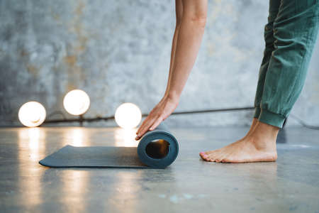 Hands roll the yoga mat on the floor. The girl puts a mat for fitness on the floor of the legs...