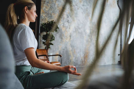 A beautiful girl in a tracksuit meditates, folding fingers into mudras. Assanas for reassurance. Relaxation by yoga and sports.Harmony with yourself. high quality photoの写真素材