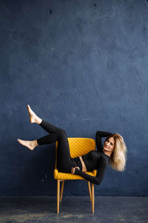 The girl poses in a yellow chair. Photo shoot in the photo studio. white hair. blue background. high quality photoの写真素材