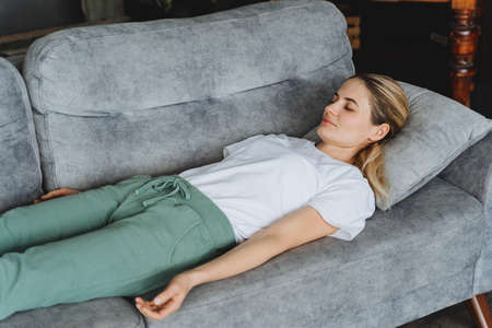 An attractive girl does yoga on the couch. Lie in the corpse position with your eyes closed. Yoga classes even at home.Complete relaxation. high quality photoの写真素材