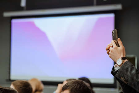 Hands with a phone shoot video in the conference room. Smartphone in a man's hand. Conduct a video...