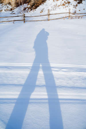 The shadow of a man in the snow, the black silhouette of the figure of a man in winter on a white background, a tourist walks through the forest casting a shadow. art fragment. high quality photoの写真素材