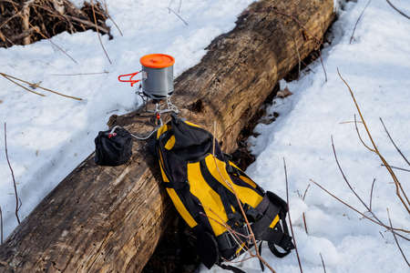 Halt parking in the forest, yellow backpack lies on the snow, burner stands on the log to prepare lunch on a hike, camping equipment, survival in the wild cold. high quality photoの写真素材
