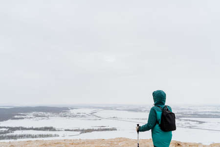 A tourist man in a green jacket stands on top of the mountain looking ahead, Nordic walking with poles, a black backpack on his back. View from the mountain, landscape. high quality photoの写真素材