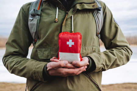 the guy holds in his hands a hiking bag, a first aid kit with medicines, a red emergency bag of first aid. Medicines in a package, red cross. high quality photoの写真素材