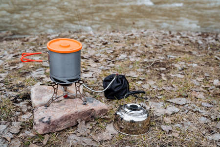 Tourist utensils, silver kettle, aluminum pot with handles and lid, gas camping burner, field kitchen, cook food in the forest. high quality photoの写真素材
