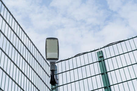 LED street lamp hanging on the fence, modern lighting of sports grounds, energy saving new technologies, lamp during the day against the sky. high quality photoの写真素材