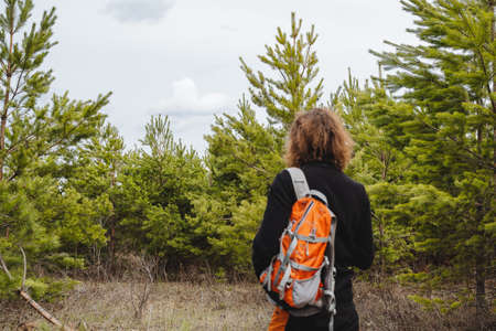 A human tourist view from behind, a backpack hanging on one shoulder, an orange travel bag, getting lost in the woods, surviving alone, lost among the trees. high quality photoの写真素材