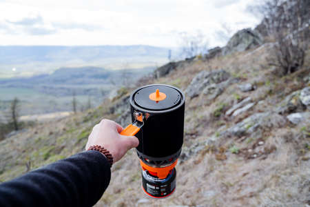 A man's hand holds a pot for eating against the backdrop of mountains, a fast food system, a safe...
