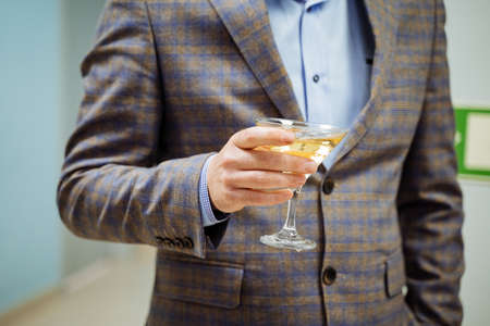 A presentable man in a jacket holds a glass of champagne in his hand, his hand took a glass of wine,...