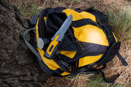 A hiking knife for survival in the forest lies on a backpack, a hiking knife with a yellow handle,...