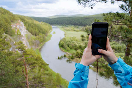 A person photographs a landscape on a phone, women's hands hold a smartphone while taking a selfie, beautiful nature in a cell phone lens. high quality photoの写真素材