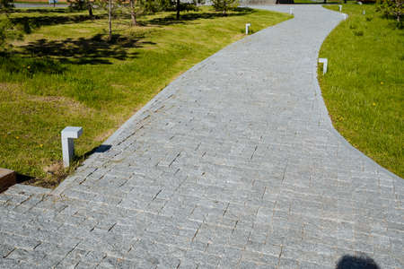 A stone road is paved with cobblestones, a road of stone bricks, a city park for walking, a pedestrian road, a mowed lawn. high quality photoの写真素材